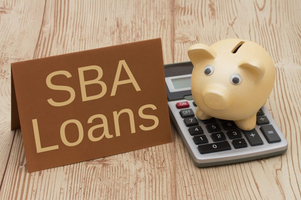 SBA loan sign beside a piggy bank and calculator, representing Small Business Administration financing and startup business loan options.