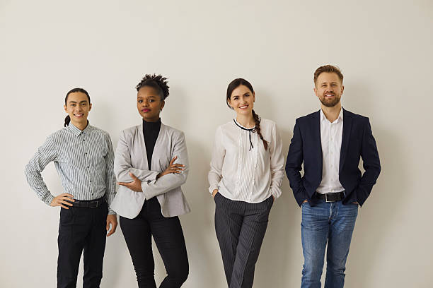 Professionally dressed business men and women wearing modern business casual clothing, standing together and smiling in a clean office setting.