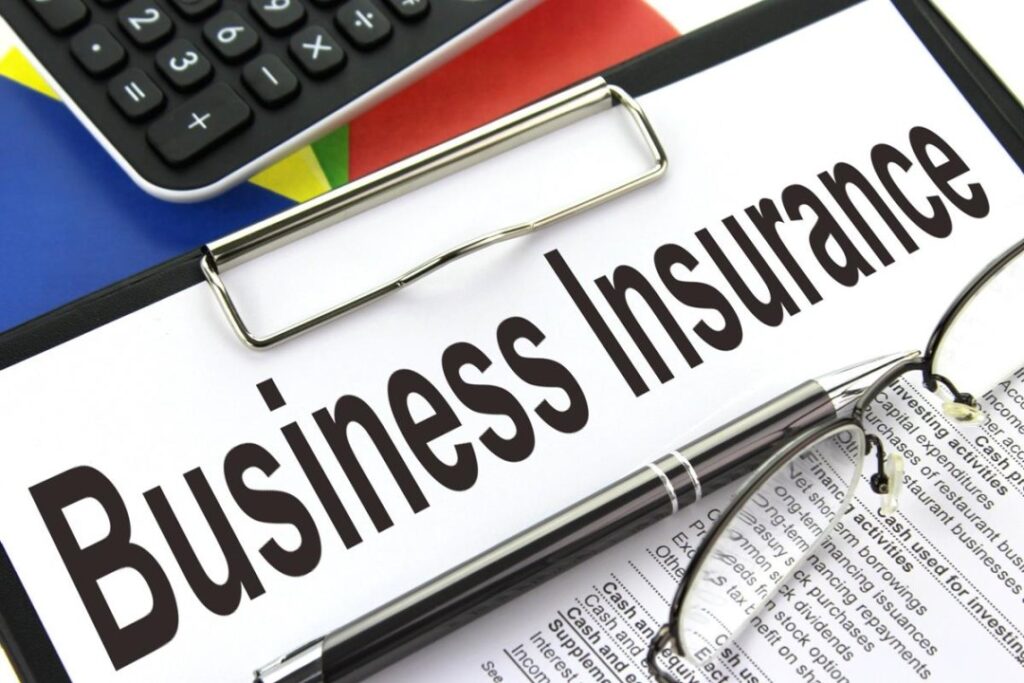 Business insurance document displayed on a clipboard with a calculator, pen, glasses, and financial papers. 