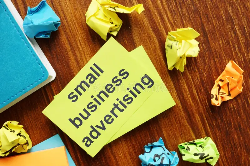 Small business advertising concept featuring a note with “small business advertising” surrounded by colorful papers on a wooden desk. 