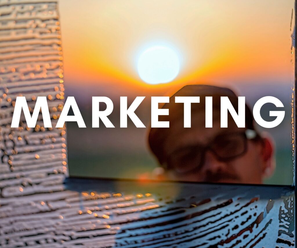 Marketing Your Window Cleaning Business: A person using a laptop at sunset with the word “Marketing” overlaid, representing digital marketing strategies to promote a window cleaning business.