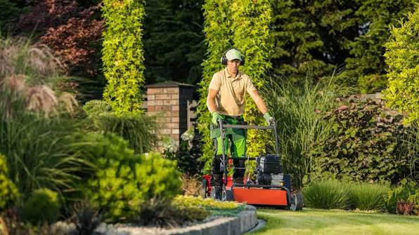 Lawn care worker wearing ear protection and gloves mowing a residential lawn with a push mower, representing a lawn care business under $1,000