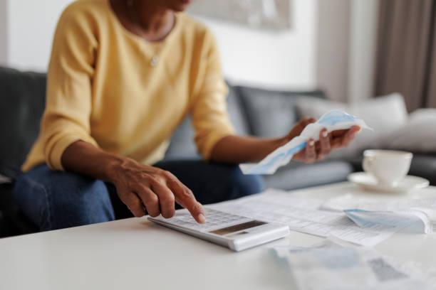 Person on a sofa using a calculator and reviewing receipts and paperwork on a white table, representing a pricing check to make sure prices cover business costs