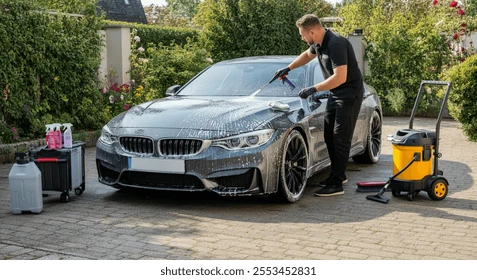 Mobile car detailer washing a sports car in a driveway with a wet/dry vacuum and cleaning supplies beside it