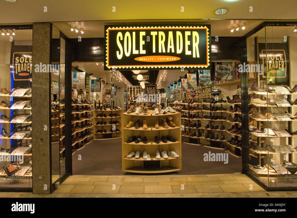 Storefront of a shoe shop named "Sole Trader" with shelves of footwear on display, a wordplay image for sole trader in the UK